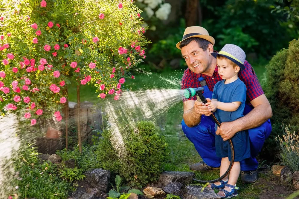 Opa und Enkel gießen Blumen