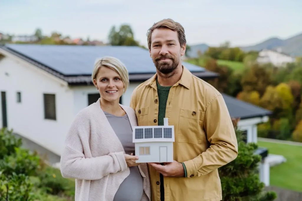 Nahaufnahme eines glücklichen Paares, das ein Papiermodell eines Hauses mit Sonnenkollektoren hält Photovoltaikanlage: Anleitung & Tipps zur Planung einer Solaranlage